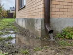 Мокрый фундамент дома и вода из водосточной трубы после дождя